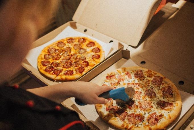 A cook slicing pizzas in open boxes